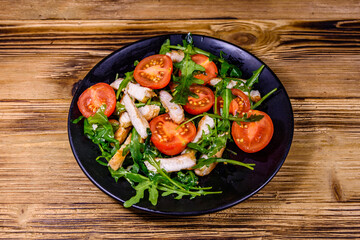 Roasted chicken breasts and salad with arugula and cherry tomatoes in a black plate