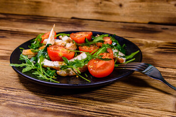 Roasted chicken breasts and salad with arugula and cherry tomatoes in a black plate