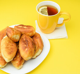 Lemon tea in a yellow ceramic mug and fried pies on a white plate, on a yellow background. The concept of a hearty breakfast and snack. Top and side view.
