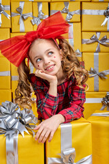 dreamy kid girl posing in studio surrounded by gift boxes celebrating birthday, rejoicing many presents. Caucasian cute child in dress shine with happiness, happy to get many gifts for holiday