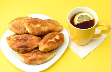 Lemon tea in a yellow ceramic mug and fried homemade pies on a white plate, on a yellow background. The concept of a hearty breakfast and snack. Top and side view.