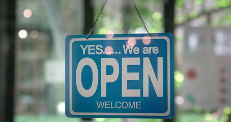 We are open, words on a signboard hanging on glass door of a restaurant. 