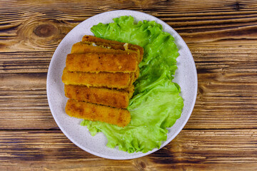 Baked fish sticks and lettuce leaves in a plate. Top view