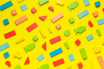 Multi-colored children's constructor made of natural wood on bright yellow background flat lay top view. Colored children's bricks for construction. Building blocks background. Developing toys, game