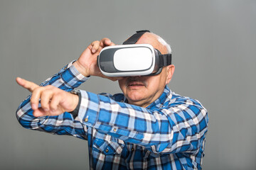 Old man in virtual reality glasses over grey background