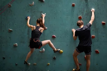 Fotobehang fitness, extreme sport and healthy lifestyle concept. young couple bouldering on rock climbing wall at indoor gym, rear view on young man and woman engaged in sport, preparing for competition © Roman