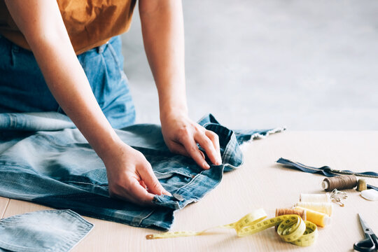 Woman repairs sews reuses fabric from old denim clothes economical reuse. DIY Hobby Reuse Recycling