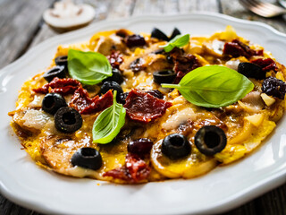 Delicious breakfast - scrambled eggs with fried white mushrooms, parmesan, sun-dried tomatoes and black olives served on wooden table
