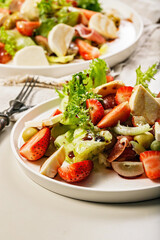 Close-up salad with jamon, strawberries, grapes, mozzarella and olives with pomegranate sauce. Healthy and balanced nutrition. Organic food. Mediterranean cuisine recipes. Vertical shot. Copy space