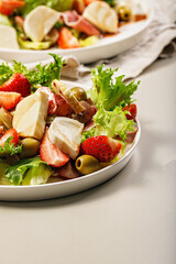 Close-up salad with jamon, strawberries, grapes, mozzarella and olives with pomegranate sauce. Healthy and balanced nutrition. Organic food. Mediterranean cuisine recipes. Vertical shot. Copy space