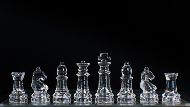Transparent glass chess pieces on a board isolated on black background