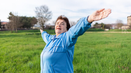 Smiling elderly caucasian woman in sports clothes, doing sports in the park. International Day of Older Persons. Concept of a healthy lifestyle and sports