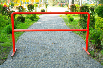 Closed entrance to the city park. There is a metal red partition at the entrance of a playground....