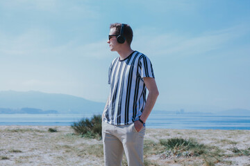 young man walking on the beach with headphones listening to music relaxed