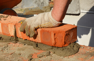 Masonry construction. A bricklayer is laying bricks on mortar using a trowel, a string line, or a level line to build a horizontal surface of the brick wall.