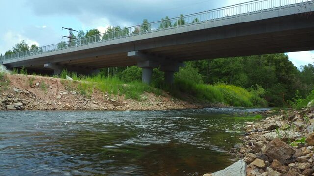 A road bridge over a shallow rough river with rapids in the middle of the forest. Unique natural places, far from civilization.