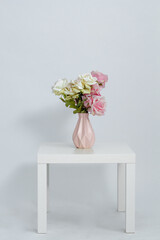 Pink vase with flowers on the table on a white background. Space for text. Close-up.	