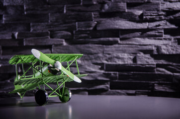 Grünes Blechflugzeug auf leicht reflektierender Oberfläche vor grauer Steinwand stehend II