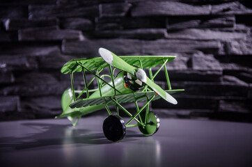 Grünes Blechflugzeug auf leicht reflektierender Oberfläche vor grauer Steinwand stehend III