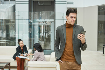 Fototapeta premium Young businessman using his mobile phone with two businesswomen communicating in the background