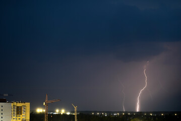 Naklejka na ściany i meble Lightning strike against the background of a dark sky. Thunderstorm in the city. 