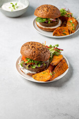 Meat free plant based burgers served with sweet potato wedges and green mix salad on gray table....