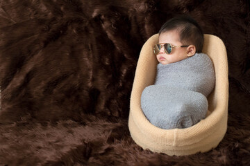 Cute Asian newborn baby wrap with grey blanket on brown fur background. Nice portrait of little child boy and glasses. sunglasses
