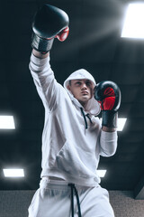 Brutal athlete boxing in the ring in a white hoodie covered with a hood. Mixed martial arts concept.