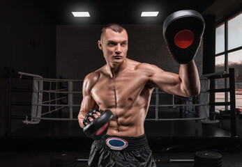 Brutal athlete holds boxing paws against the background of the ring. Mixed martial arts concept.