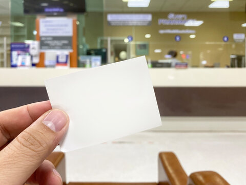 Young Man Hand Holding Blank Cue Card With Blurred Cashier Counter Background, Young Man Showing Blank Ticket Card And Waiting For The Queue