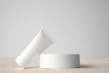 Mockup luxury facial skincare white tube bottle product with blank label leaning on white round pedestal or display against sandy white plain light grey background copy space. Minimal design concept