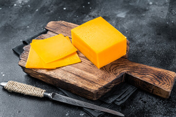 Slices of Cheddar Cheese on a wooden cutting board. black background. Top view - obrazy, fototapety, plakaty