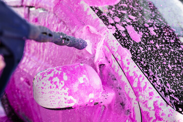 Gun sprinkles pink foam on car at self-service car wash. Unusual