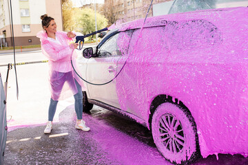 Car in pink foam at self-service car wash, woman worker happily doing her job
