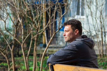 Naklejka na ściany i meble Attractive brunet pensive man, sitting on the bench, enjoying spring weather