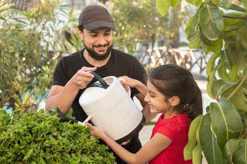 Gardener smiles and teaches her daughter while watering the plants and shrubs in her backyard on a spring day