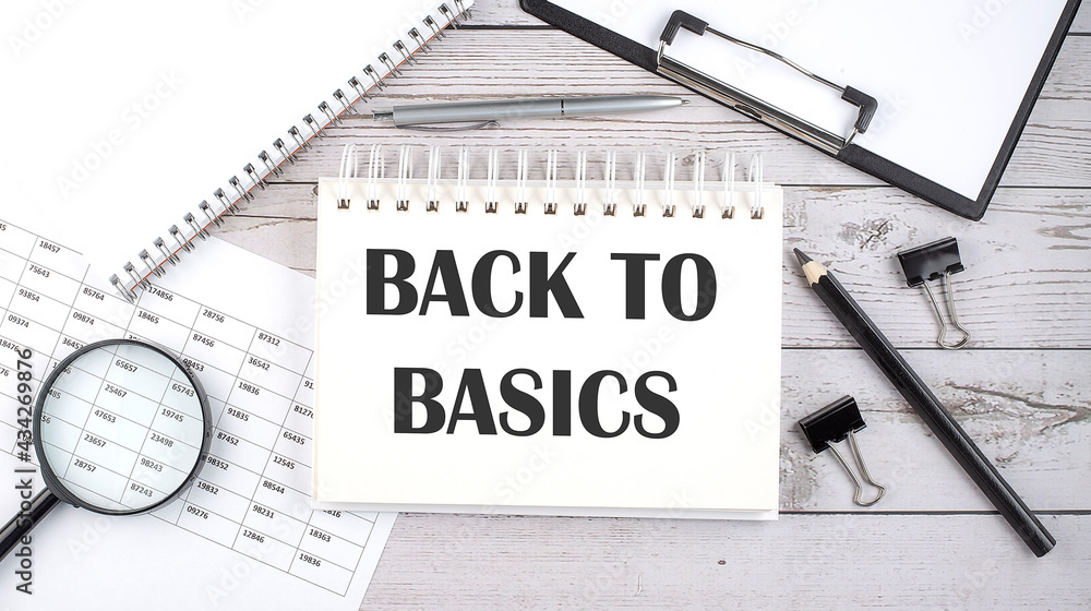 Poster notepad with text backto basics with a pen,office tools and graphs on the desktop.