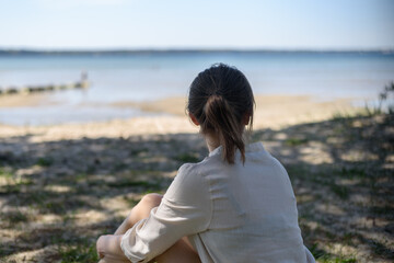 Woman in linen clothes sitting between pine trees and looking to sea. Wellbeing, mental health