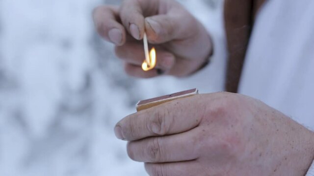 Closeup of crop male traveler lighting match in snowy forest in winter 