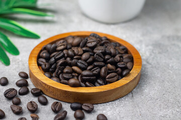 Biji Kopi or Coffee beans on wooden plate, with a cup of cappuccino and coffee beans on grey background. Top view. Copy space for text.