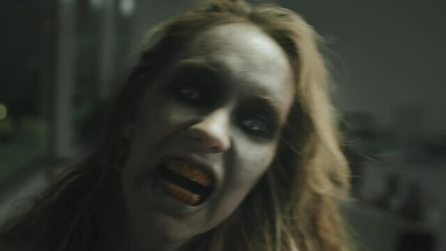 Close up tracking shot of angry zombie woman with SFX makeup and stained teeth grunting and walking towards camera
