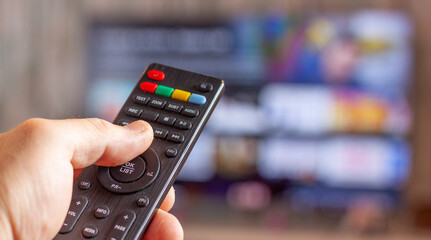 vista de una mano con un mando a distancia con una  televisión delante con una aplicación de cine y series