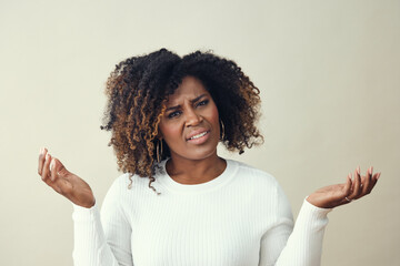 Uncertain African American Woman Looking at the camera while gesturing with hands raised on her...