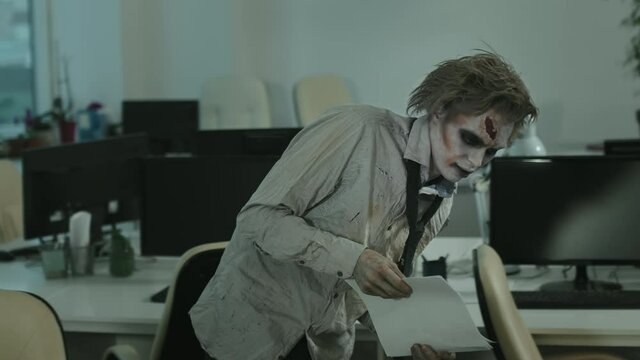 Tracking shot of zombie businessman in dirty and torn shirt with necktie and SFX makeup with fake wound holding documents and walking in office