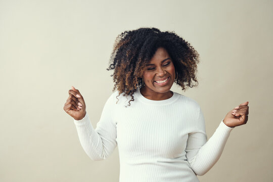 Cheerful woman with frizzy hairstyle dancing against white background