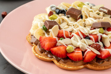Heart waffle with banana and strawberry with gummy candy and ice cream on it.