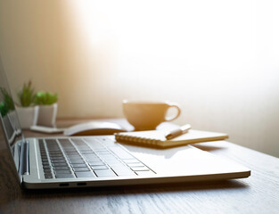 Fototapeta premium soft focus of Office desk table with keyboard of laptop computer, coffee cup and notebook, glasses. Business and finance concept. Workplace with morning sunlight from window with copy space.