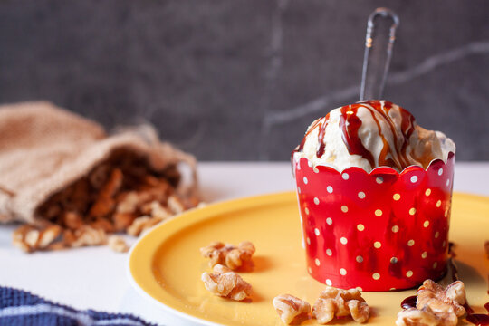 Vista de una tarrina de helado de vainilla con nueces de pecan con algunas nueces derramadas alrrededor de la tarrina sobre un plato amarillo