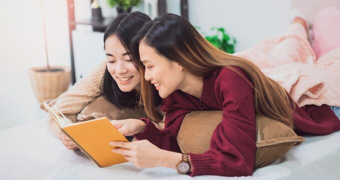 Young beautiful Asian women lesbian couple lover reading book in living room at home with smiling face.Concept of LGBT sexuality with happy lifestyle together.