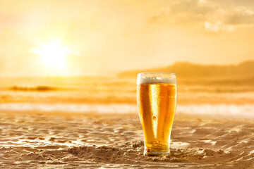 Glass with fresh beer on the sand golden sunset background